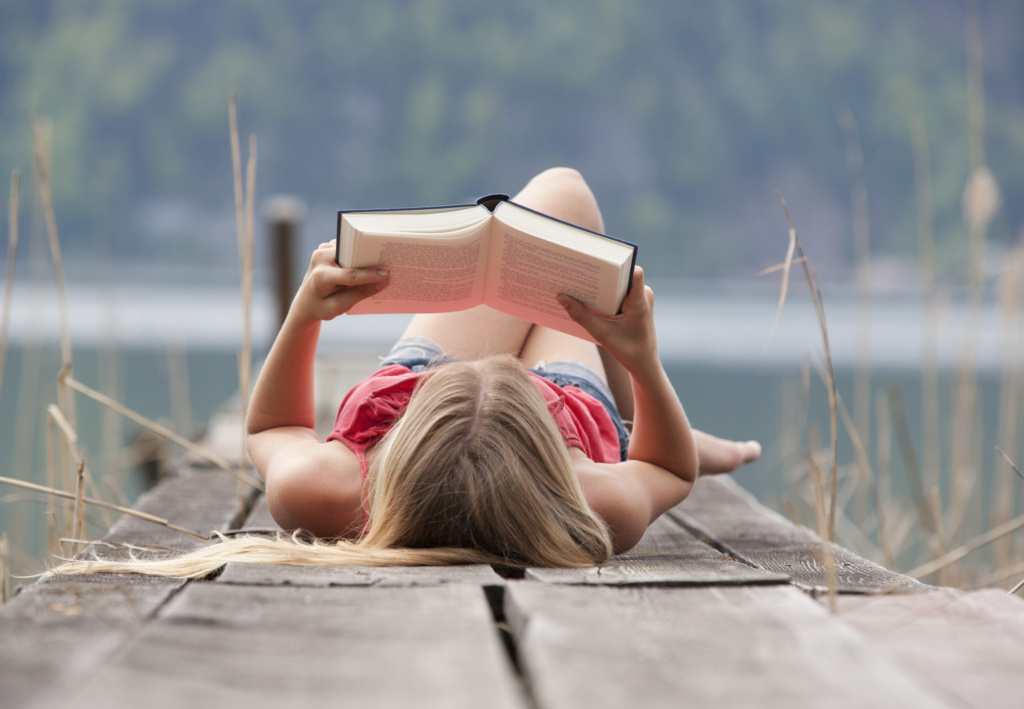 Austria, Teenage girl lying and reading book on jetty